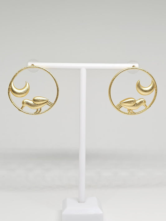 Brass hoop earrings with bird and crescent moon design on display stand.