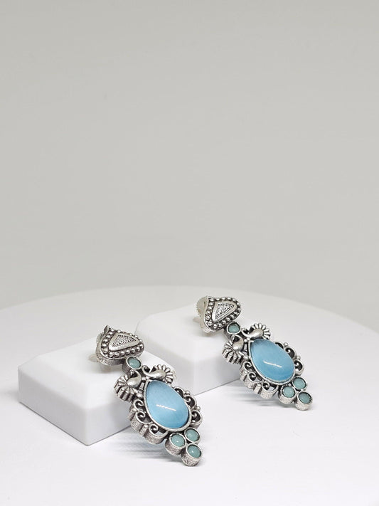 Elegant silver-tone dangle earrings with blue teardrop stones and intricate antique detailing.