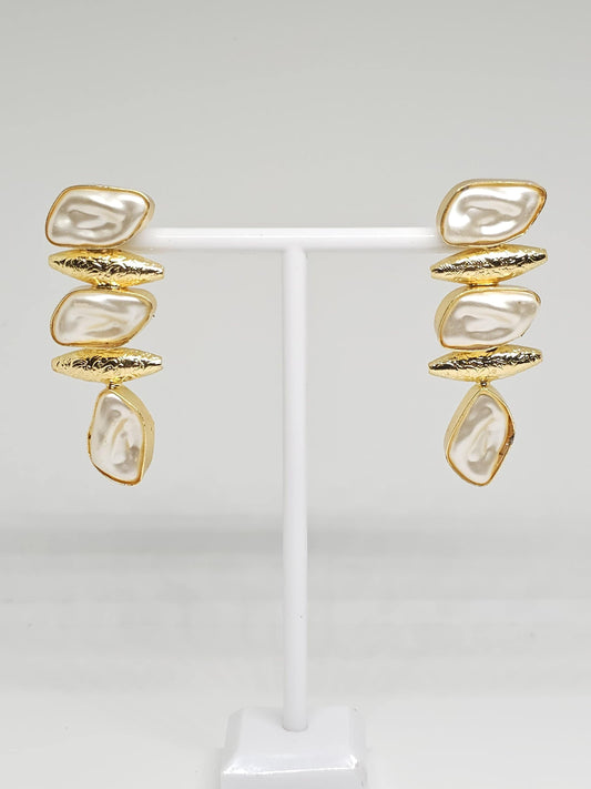 Gold-tone drop earrings with irregular mother of pearl stones on a white stand